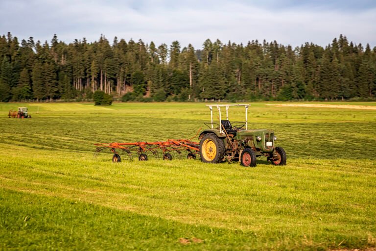 Agricultural machinery, a tractor collecting grass in a field against a blue sky. Season harvesting, grass, agricultural land. Selective focus